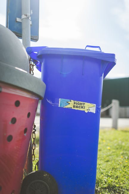 A person is seen disposing of a crumpled brown paper bag into a white rubbish bin, which is partially open, revealing a similar paper bag inside. The individual’s arm is extended, holding the bag over the bin, and they are wearing a short-sleeved garment. The bin is situated on a flat surface, possibly a wooden table or countertop, and the environment appears to be indoors with a clean, modern setting. Additional crumpled paper bags are visible in the foreground, some on the surface near the bin. The scene reflects an aspect of domestic waste disposal, highlighting the process of on-site rubbish removal in a residential context, aligning with waste management services provided by Waste Removal Sutton, especially in relation to the handling of paper-based waste materials applicable to private collection or alternative waste handling methods.